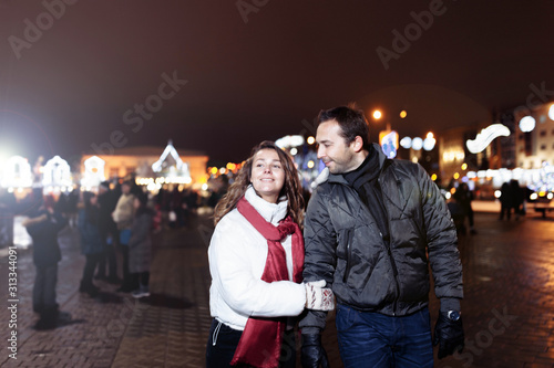 Loving couple on a date in a festive city with New Year's lights in the winter evening. Spouses in winter clothes Christmas.