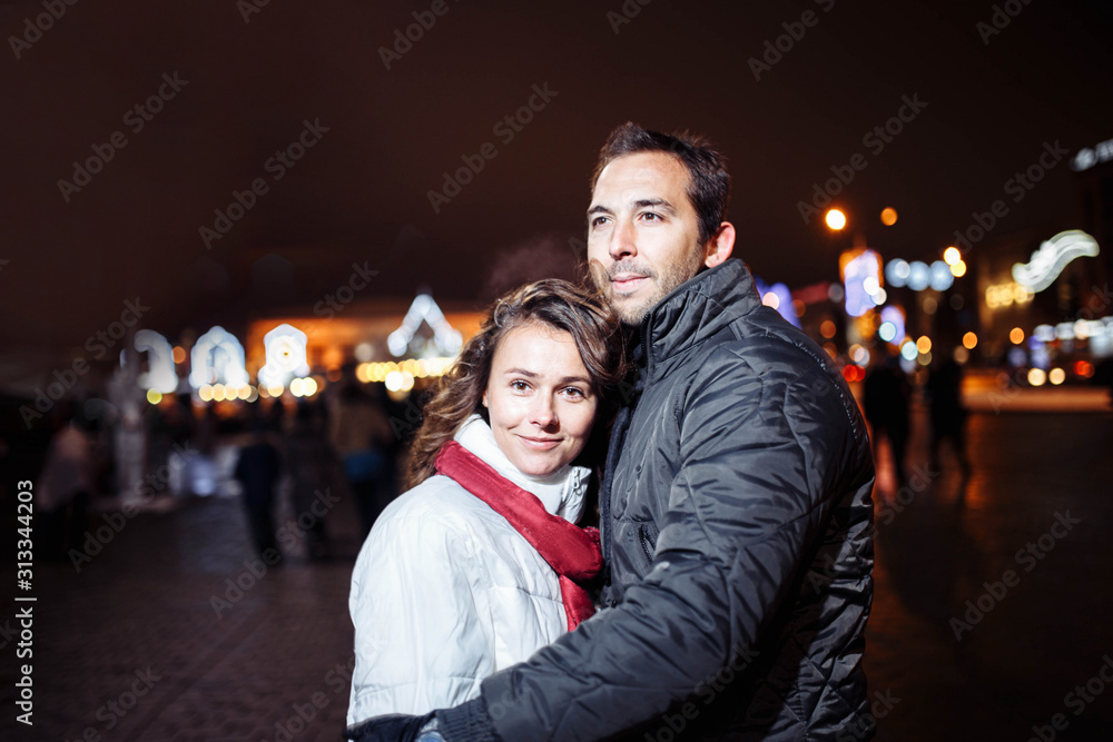 Loving couple on a date in a festive city with New Year's lights in the winter evening. Spouses in winter clothes Christmas. Loving couple on a date in a festive city with New Year's lights in the winter evening. Spouses in winter clothes Christmas.