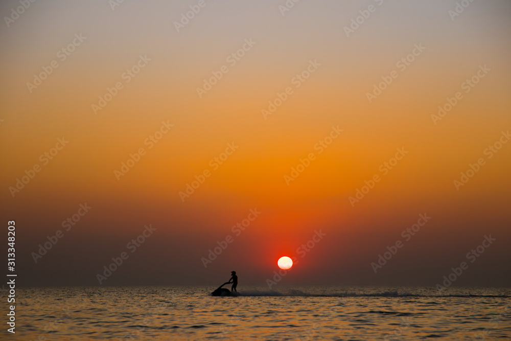 Silhouette of a man on a jet ski in the sea with sunset.