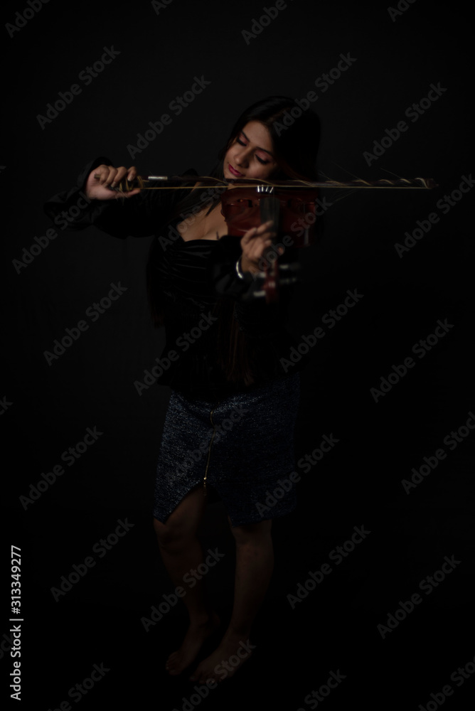 Fashion portrait of an young and attractive Indian Bengali brunette girl with black western dress is playing violin in front of a black studio background. Indian fashion portrait and lifestyle. Fashion portrait of an young and attractive Indian Bengali brunette girl with black western dress is playing violin in front of a black studio background. Indian fashion portrait and lifestyle.