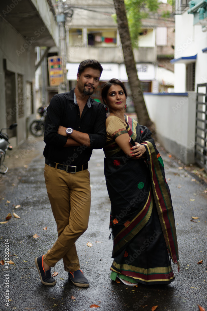 A brunette Indian Bengali romantic couple in traditional wear interacting between themselves in the drenched street in the morning of Durga Puja festival in urban background. Indian lifestyle.