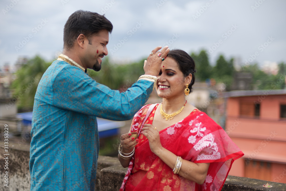 A brunette Indian Bengali romantic couple in traditional wear interacting between themselves on a roof top in romantic mood in the morning of Durga Puja festival in urban background. Indian lifestyle. A brunette Indian Bengali romantic couple in traditional wear interacting between themselves on a roof top in romantic mood in the morning of Durga Puja festival in urban background. Indian lifestyle.