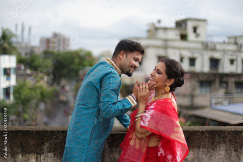A brunette Indian Bengali romantic couple in traditional wear interacting between themselves on a roof top in romantic mood in the morning of Durga Puja festival in urban background. Indian lifestyle.