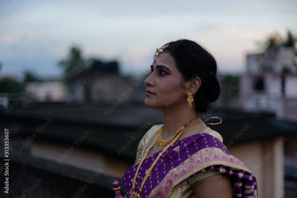 Portrait of a beautiful smiling brunette Indian Bengali bride in traditional sari standing on the roof top in afternoon under blue sky. Indian lifestyle.