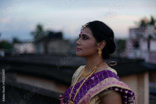 Portrait of a beautiful smiling brunette Indian Bengali bride in traditional sari standing on the roof top in afternoon under blue sky. Indian lifestyle.