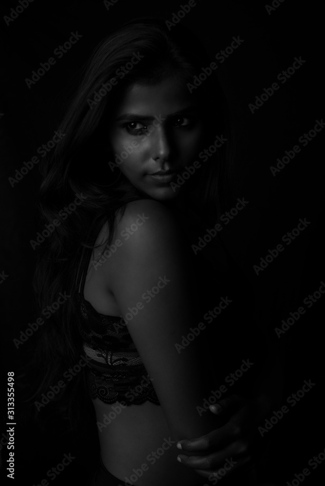 Monochrome fashion portrait of an Indian brunette Bengali dark skinned woman with black lingerie standing in black studio copy space background. Indian fashion photography and lifestyle.