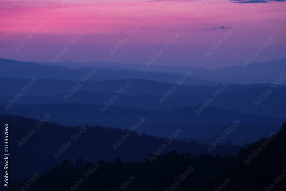 Nature landscape background beautiful view of the morning fog filling the valleys of smooth hills mountain range layer dark blue forest sunrise and sunset in mountains with purple sky dramatic /
