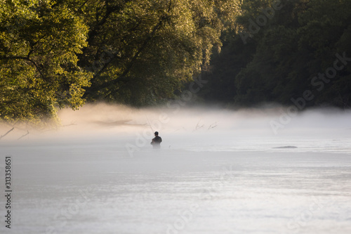 A lone fly fisherman enjoys the river on a foggy summer morning.