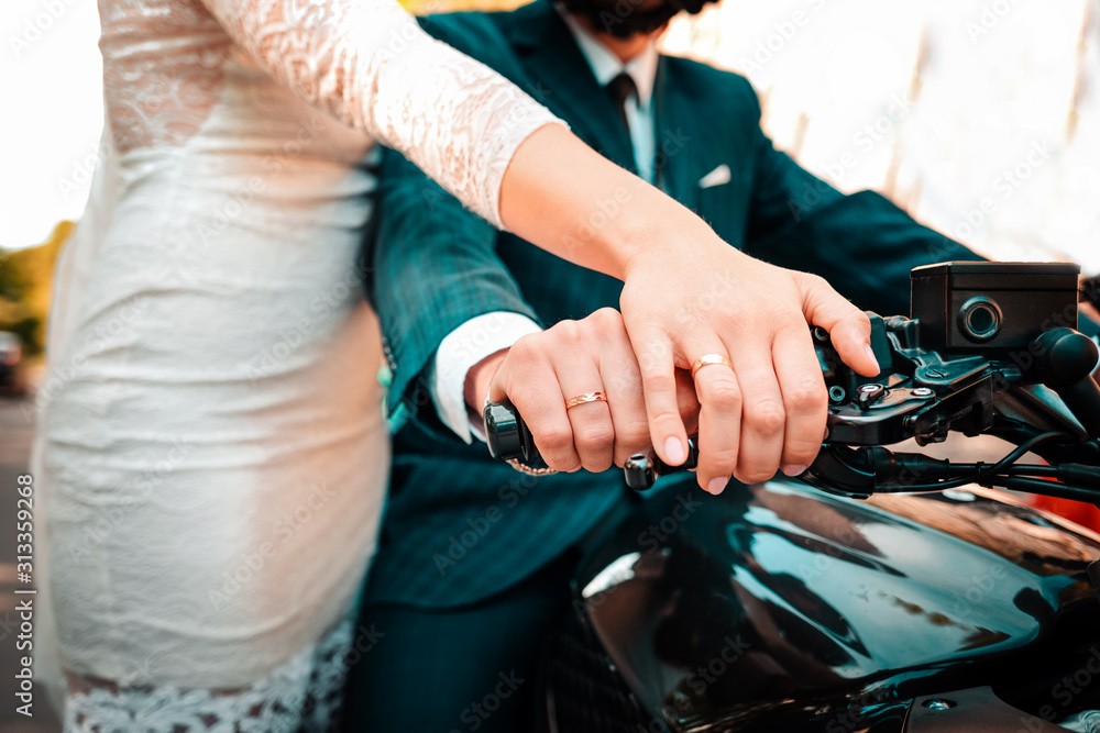 Wedding, newlyweds. A man and a woman in wedding attire hold on to a motorcycle handle, showing off their engagement rings. Hands close up