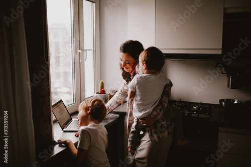 Busy mom with two children works on laptop kitchen photo