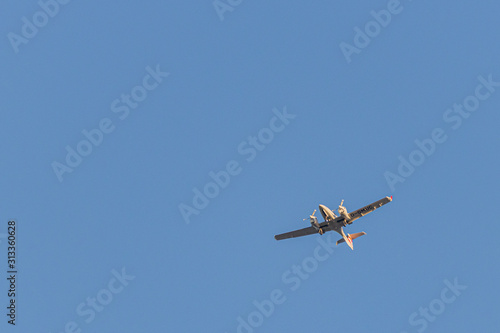 a twin-engined small airplane flies in the blue cloudless sky