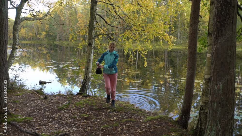 A young woman draws water from a forest lake and makes coffee on an open fire. Two female friends enjoying the silence and fresh air during a hike in Finland