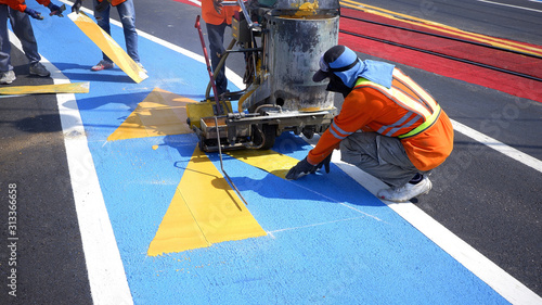 Road workers group in reflective vests with thermoplastic spray road marking machine are working to paint traffic lines and sign on asphalt road surface in the city, selective focus
