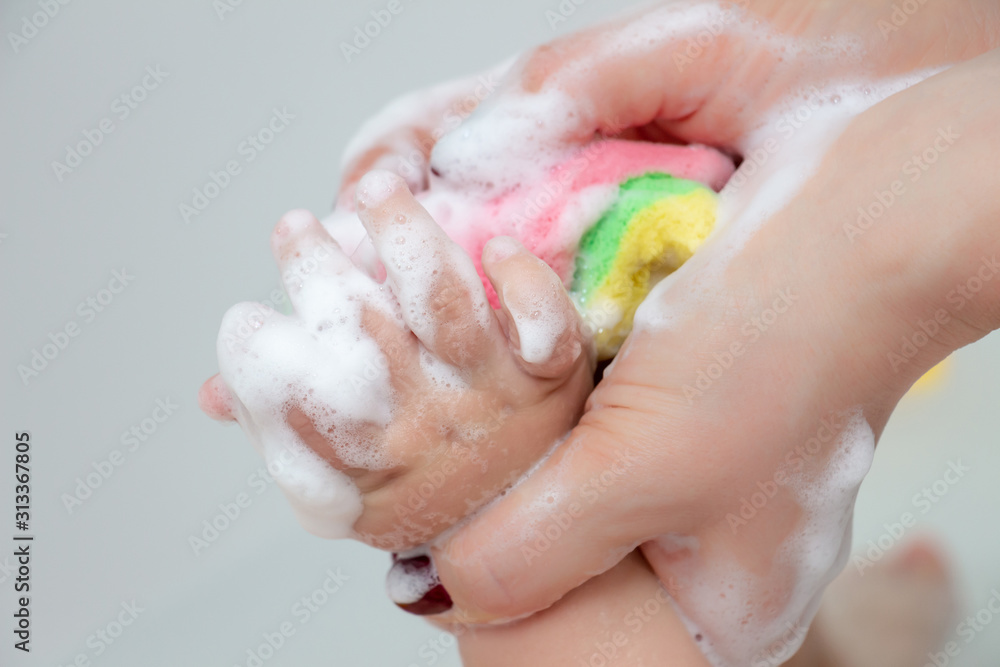 Fototapeta premium Care and cleanliness concept. Daily washing of the child. A small leg in the hands of the mother, close-up. Bathing for children