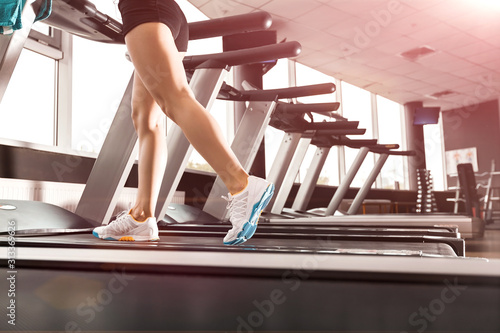 close up womans legs running at the treadmill in the gym over sunrise. wearing in white orange blue sneakers. Cardio exercise