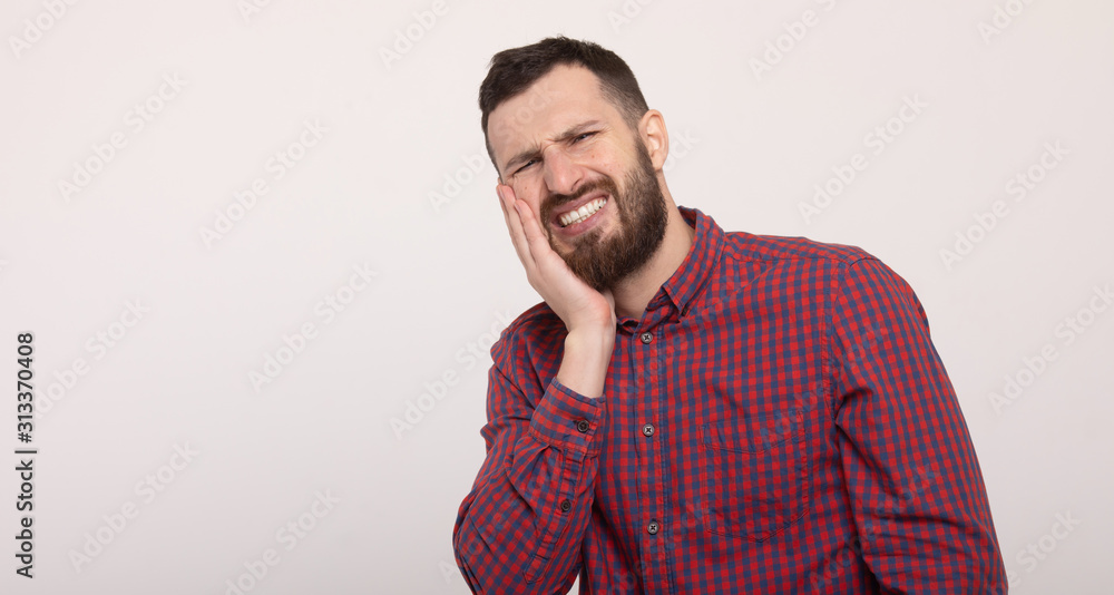 Toothache concept. Indoor shot of young man feeling pain, holding his cheek with hand, suffering from bad tooth ache. L Toothache concept. Indoor shot of young man feeling pain, holding his cheek with hand, suffering from bad tooth ache. L