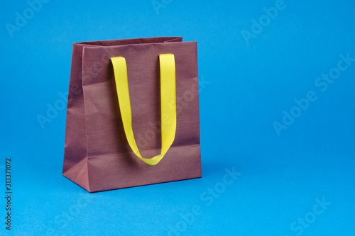 Brown paper gift bag with yellow handles on a blue background.