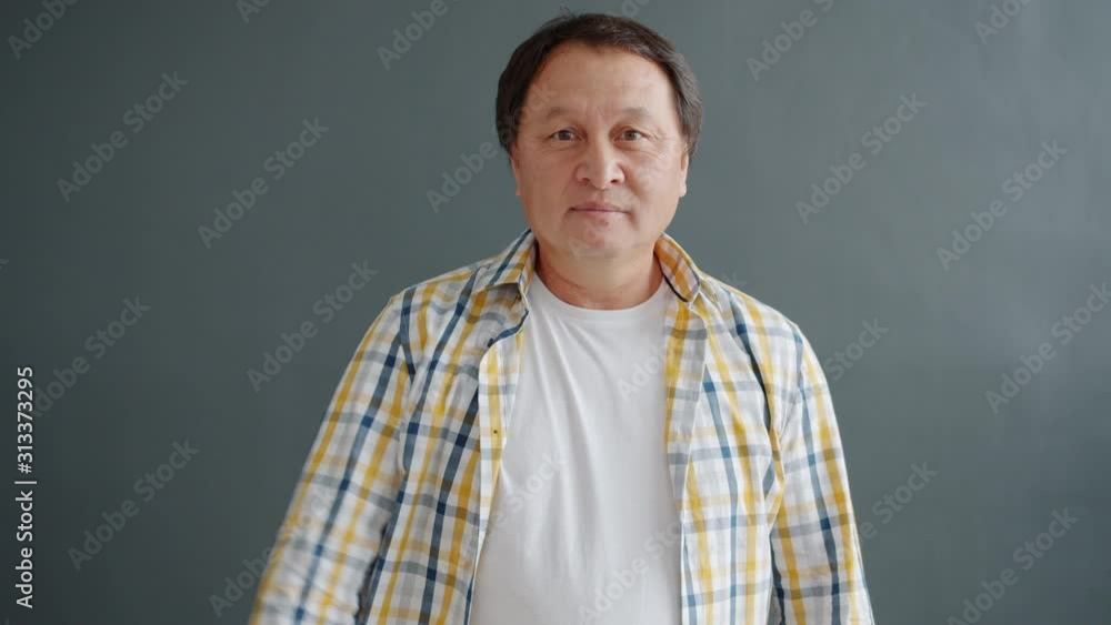 Slow motion of unhappy Asian man showing thumbs-down gesture on gray background expressive disappointment and disapproval. People and reactions concept. Slow motion of unhappy Asian man showing thumbs-down gesture on gray background expressive disappointment and disapproval. People and reactions concept.