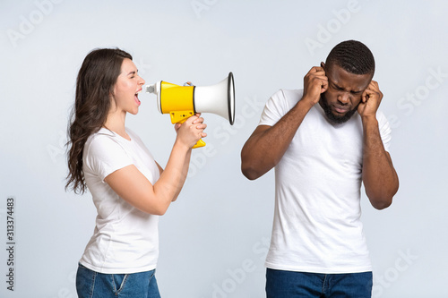 Irritated young woman screaming with megaphone at her man