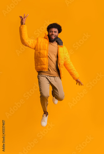 Excited afro man in bright winter jacket jumping up
