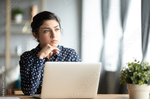 Serious thoughtful indian sit with laptop thinking of inspiration ideas