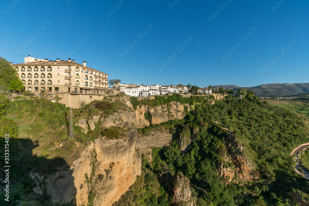 ronda village at the edge of cliffside with trees and white houses against sky, Andalusia, Spain