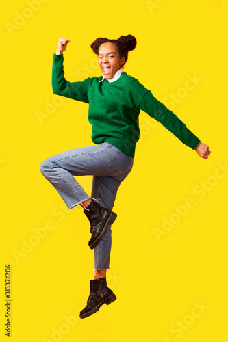 Cheering afro teen jumping over yellow background