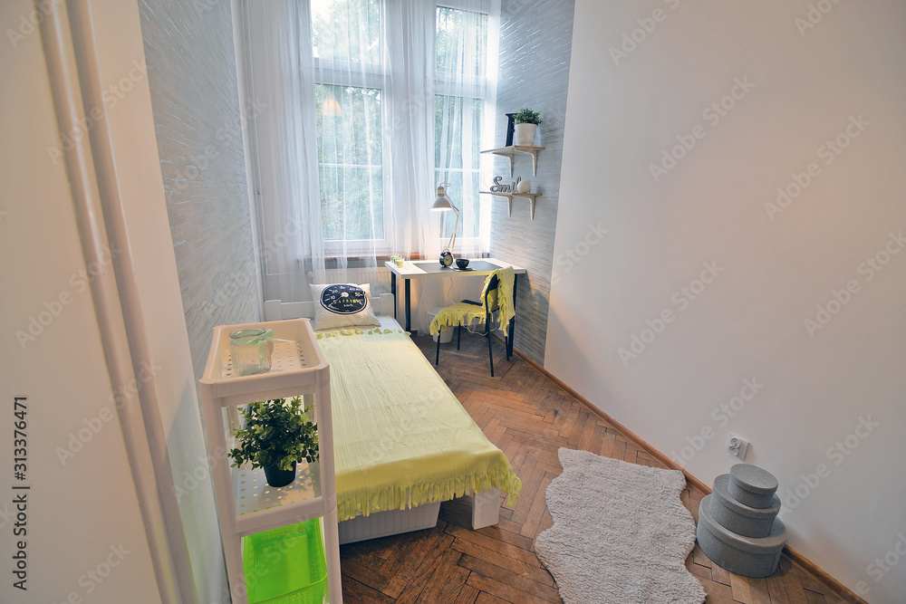 A teenager's room with a bed , wallpaper on the wall and a school desk.