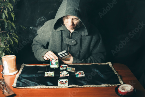 fortune telling on tarot cards. at the table, a witch in a gray hoodie makes a layout with tarot cards..