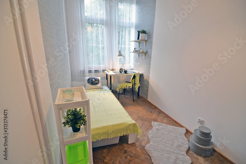 A teenager's room with a bed , wallpaper on the wall and a school desk.