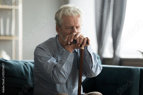 Depressed disabled retired man sitting on couch with cane stick Fototapete