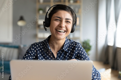 Cheerful indian woman wear wireless headset laughing with laptop photo