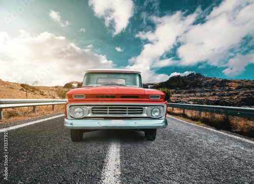 A Classical automobile on a journey on the country raod against the cloudy and blue sky
