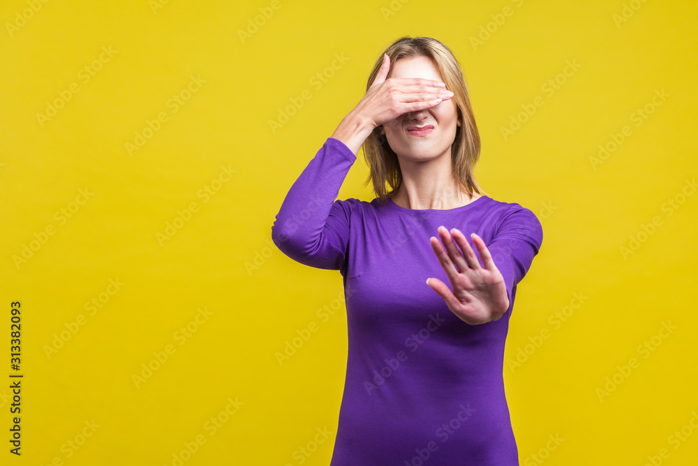 Don't want to see! Portrait of dissatisfied woman in elegant tight purple dress covering eyes with hand and gesturing stop, feeling ashamed or scared. indoor studio shot isolated on yellow background Don't want to see! Portrait of dissatisfied woman in elegant tight purple dress covering eyes with hand and gesturing stop, feeling ashamed or scared. indoor studio shot isolated on yellow background