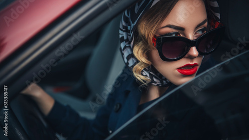 Beautiful brunette sexy spy agent (killer or police) woman in leather jacket and jeans with a gun in her hand driving a car after someone, to catch him