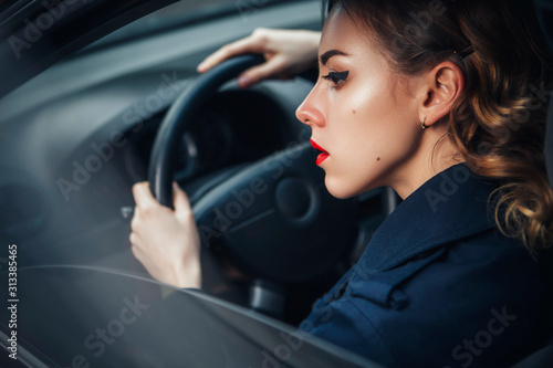 Beautiful brunette sexy spy agent (killer or police) woman in leather jacket and jeans with a gun in her hand driving a car after someone, to catch him