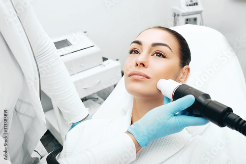 Tableau sur toile Beautician using an acoustic wave machine rejuvenates the skin of a woman's face