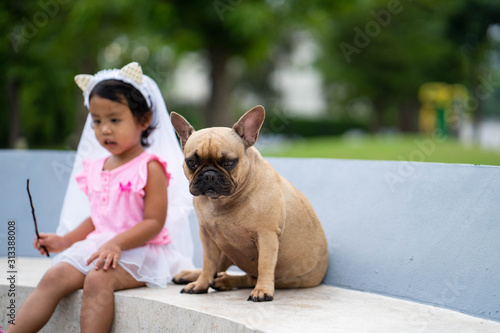 Cute asian girl playing with her lovely french bulldog at marble seat in park.