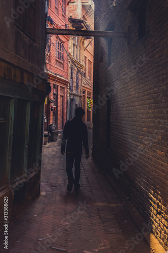 man walking down an narrow alley in a beam of light