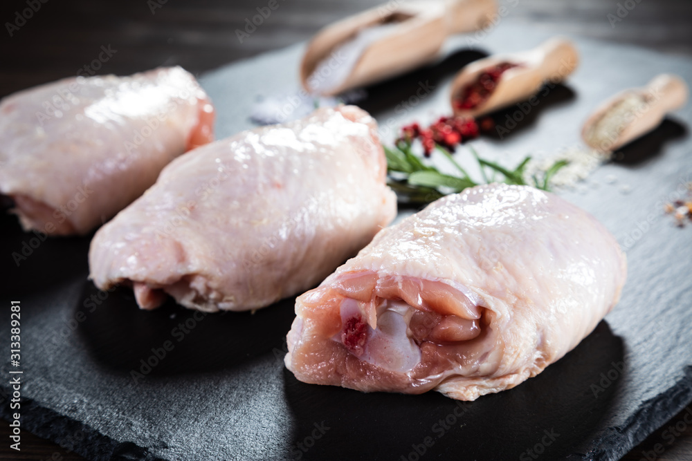Raw chicken thigs on black stone on wooden background Raw chicken thigs on black stone on wooden background