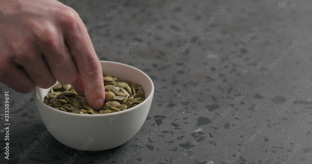 man hand takes pumpkin seeds from white bowl with copy space