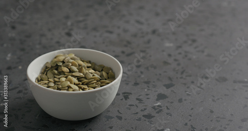 pumpkin seeds in white bowl on terrazzo countertop with copy space