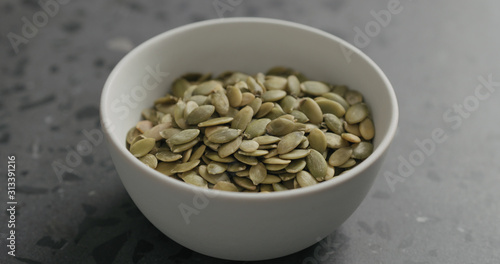 closeup pumpkin seeds in white bowl on terrazzo countertop