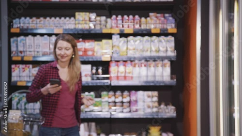 Wallpaper Mural Happy american woman using mobile phone while walking in grocery shop. Smiling female customer holding smartphone in hand, watching screen, having shopping time in supermarket. Concept: business Torontodigital.ca