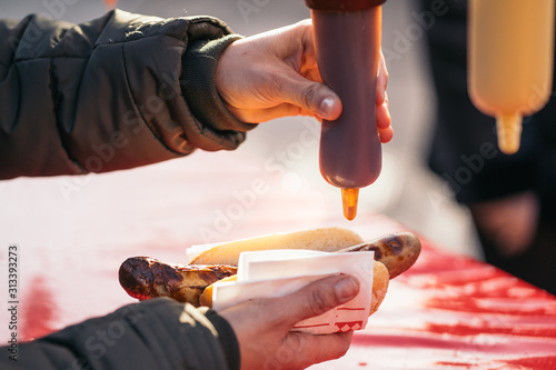 Photography Woman pouring tomato sauce, mayonnaise and mustard on a grilled pork sausage Bratwurst at a German Market