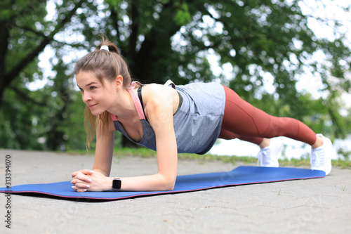 Sport girl doing plank exercise outdoor in the park warm summer day.