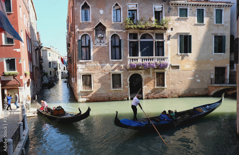 Venetian gondolier punting gondola through canal waters of Venice Italy