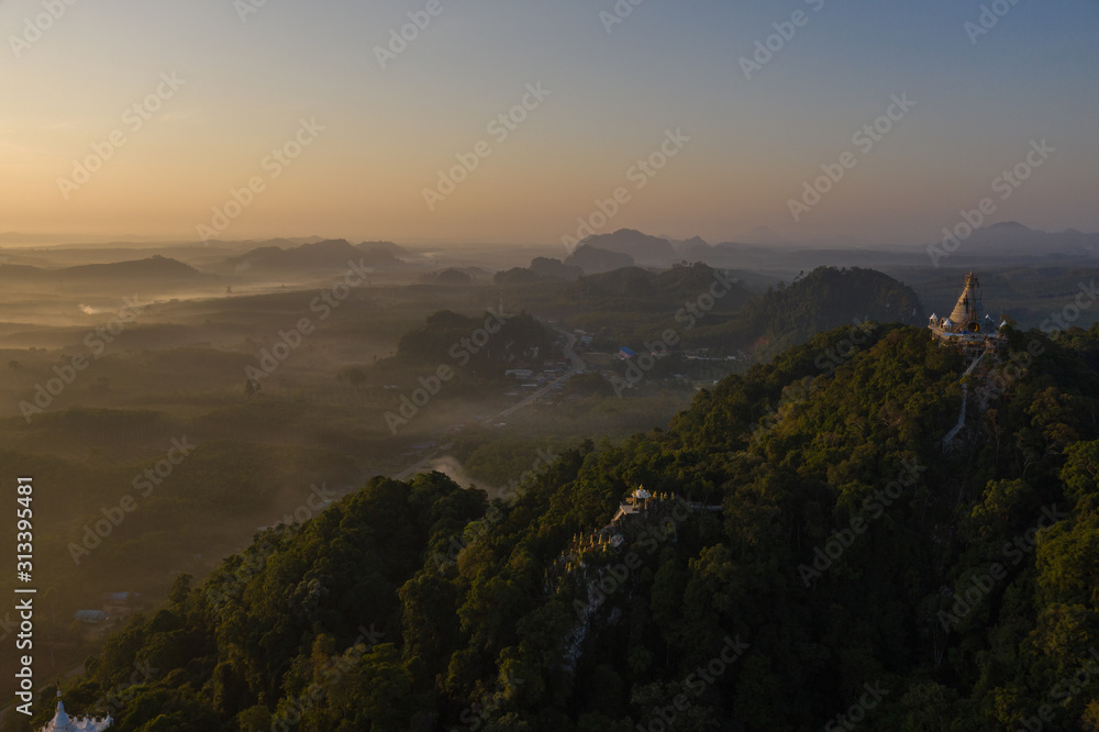 Fototapeta premium Beautiful sunrise with pagoda on the top of rock and tree with fog at Khao Na Nai Luang Dharma Park,Surat thani province,Thailand
