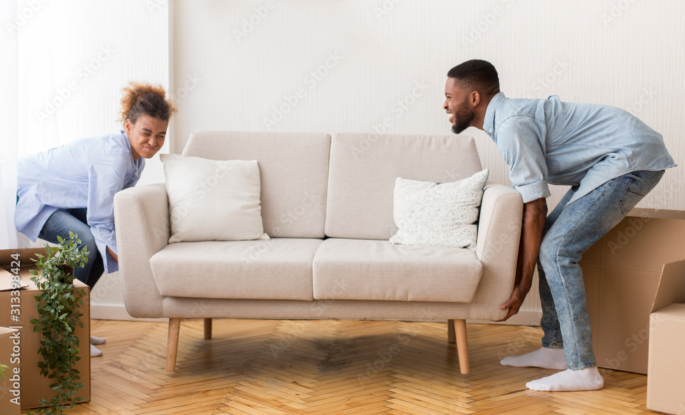 Couple Lifting Sofa Standing In Empty Room After Moving House