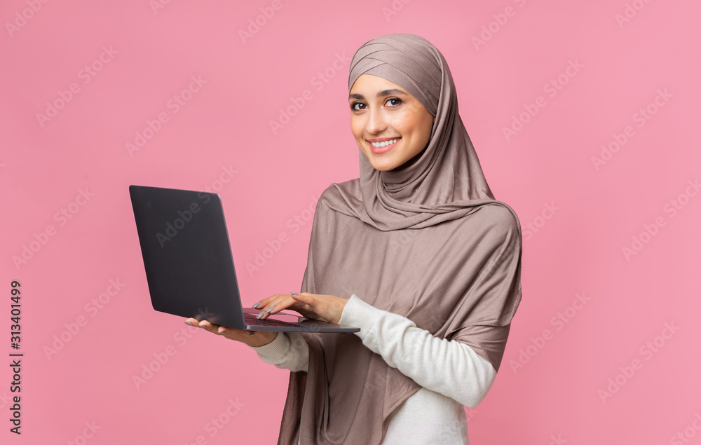 Smiling muslim woman holding laptop and looking at camera Smiling muslim woman holding laptop and looking at camera